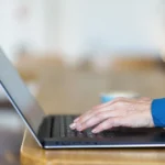 Dłonie dojrzałej osoby piszącej na klawiaturze laptopa – praca zdalna po 40 roku życia.