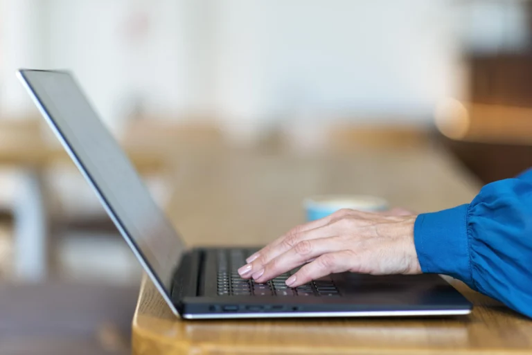 Dłonie dojrzałej osoby piszącej na klawiaturze laptopa – praca zdalna po 40 roku życia.